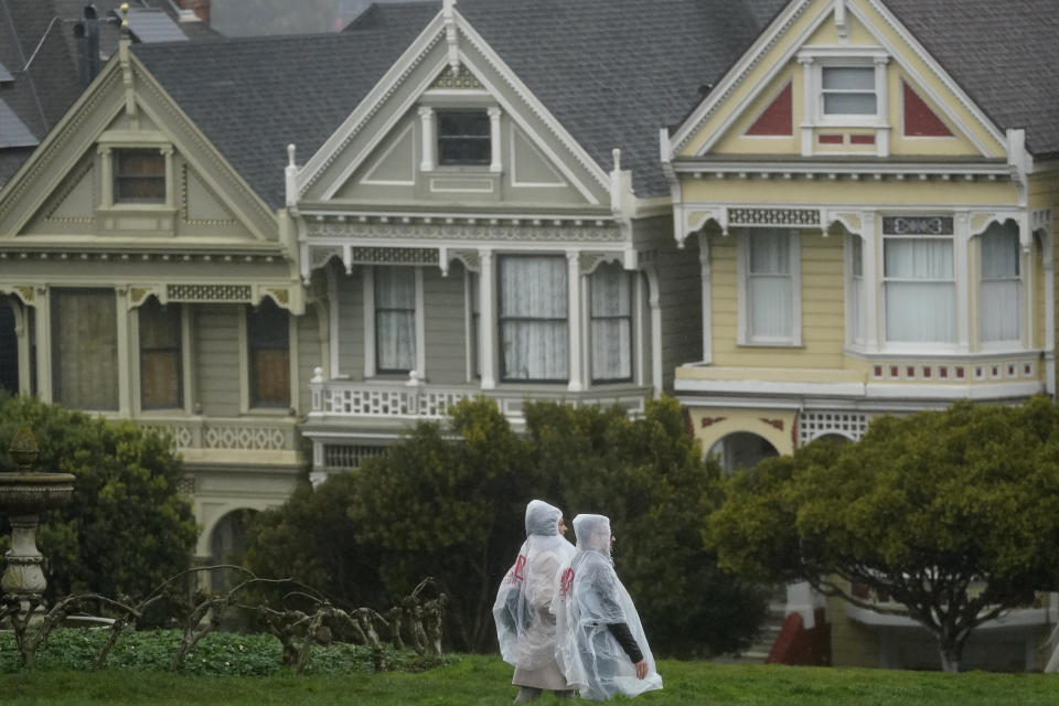 Pedestrians wearing ponchos walk down a path at Alamo Square Park in front of the "Painted Ladies," a row of historical Victorian homes, in San Francisco, Tuesday, March 21, 2023. (AP Photo/Jeff Chiu)