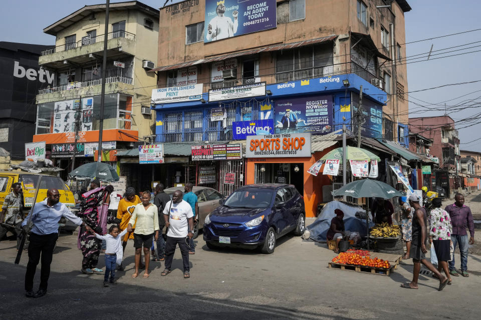 People walk past sports betting shops on a street in Lagos, Nigeria, Monday, Dec. 5, 2022. Although sports betting is a global phenomenon and a legitimate business in many countries, the stakes are high on the continent of 1.3 billion people because of lax or non-existent regulation, poverty and widespread unemployment. (AP Photo/Sunday Alamba)