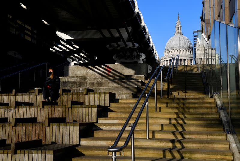 FILE PHOTO: A woman wearing a protective face mask sits in the winter sunshine with St. Paul's Cathedral seen behind amidst a lockdown during the spread of the coronavirus disease (COVID-19) pandemic, London, Britain