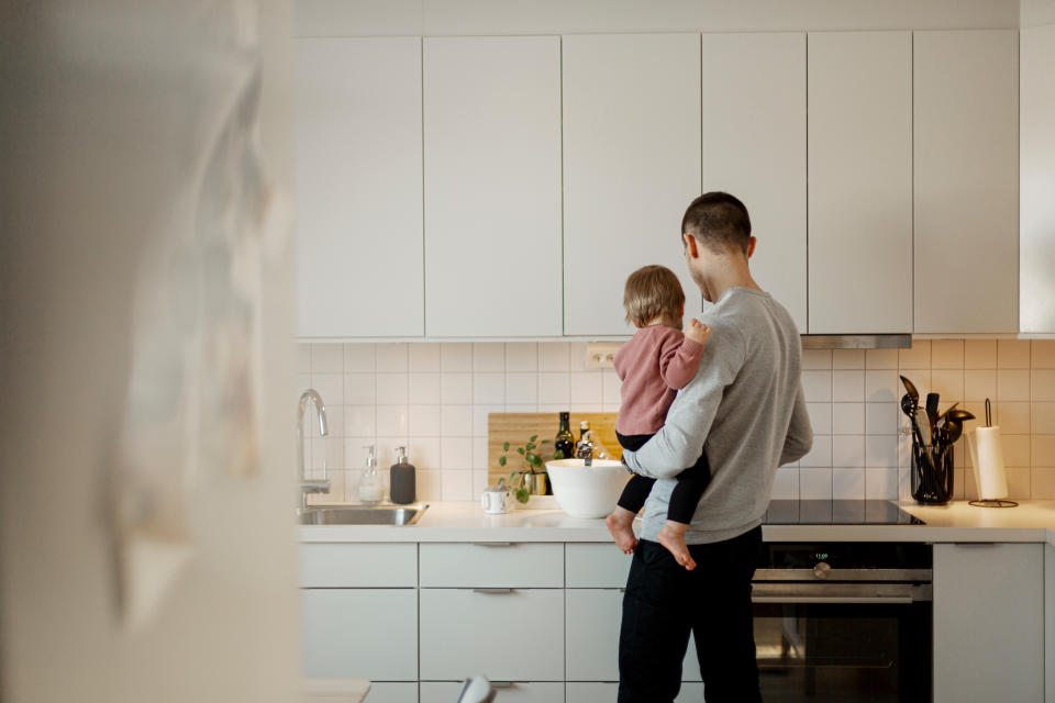 Adult holding a child in a kitchen, both facing away from the camera