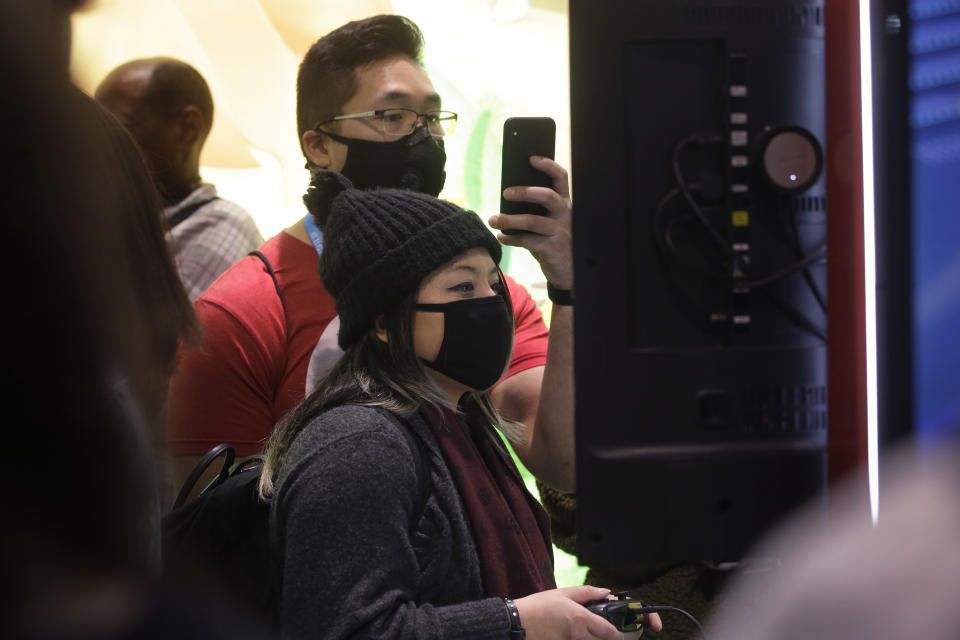 Sonya Tran, of Randolph, Mass., front, and Bobby Ratanasim, of Providence, R.I., behind center, wear protective masks while playing a Nintendo game, Thursday, Feb. 27, 2020 at the Pax East conference, in Boston. Tran and Ratanasim said concerns about the coronavirus played a role in wearing masks to the conference. (AP Photo/Steven Senne)