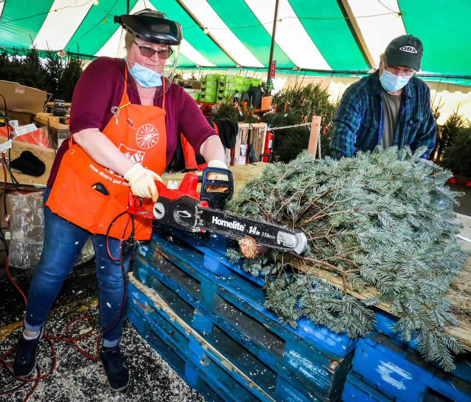 Mattina Mende makes a fresh cut on the bottom of a Christmas tree for customer Scott Ortengren, right, on Dec. 1 at the Home Depot. While big box stores are not experiencing shortages or delivery issues, local sellers are.