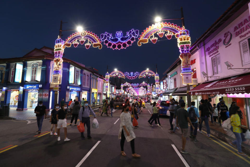 People wearing facemasks as a precaution against the spread of covid-19 cross a street decorated with festival lights ahead of Deepavali in Little India district. 