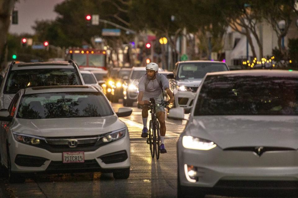 A person rides a bike in heavy evening traffic along Santa Monica Blvd