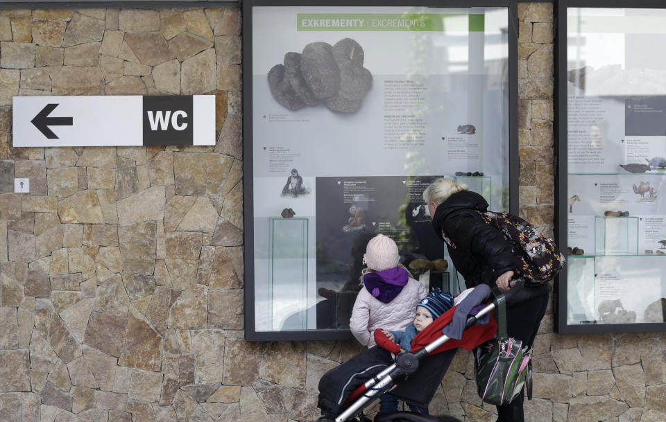 In this picture taken on Monday, May 6, 2019, visitors view an exhibition of animal excrements at the Prague Zoo, Czech Republic. The park has opened a new permanent exhibition that put on display wide range of animal feces. Placed on the outside walls of a new building with toilets, the exhibition offers information and samples from fossil turds, also known as coprolites, to the excrements of current animals of various size, shape, texture and color. (AP Photo/Petr David Josek)