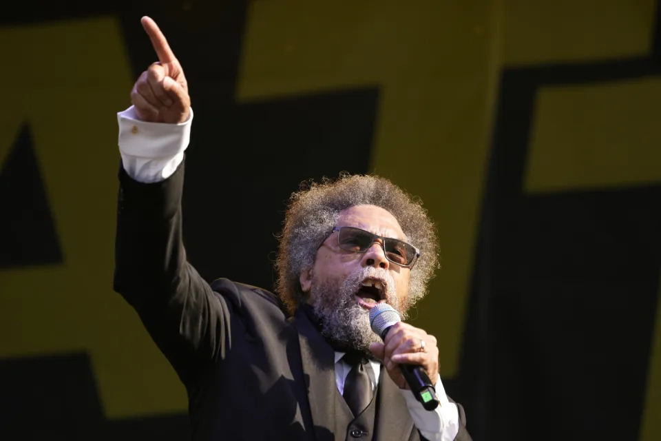 Cornel West points into the air as he speaks into a microphone.