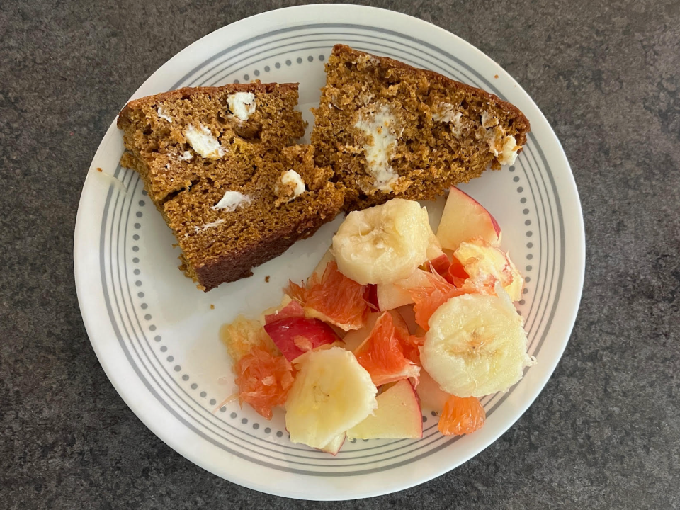 two pieces of buttered pumpkin bread on a plate with a side of fruit salad