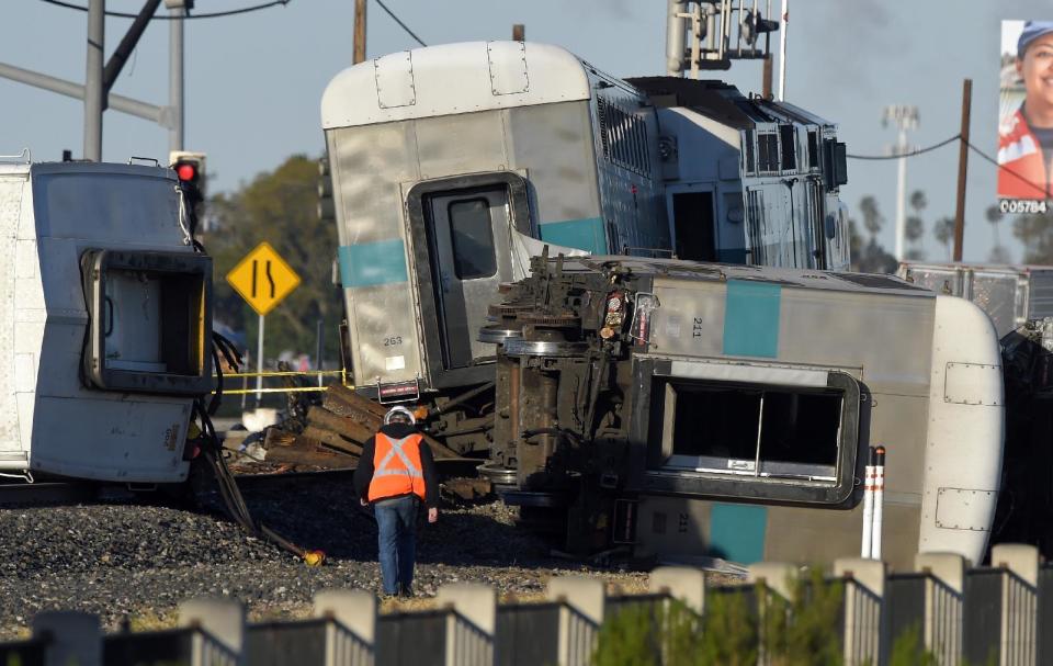 FILE - In this Feb. 24, 2015 file photo, a worker walks along the tracks near the wreck of a Metrolink passenger train that derailed in Oxnard, Calif. Federal investigators have determined that the crash that killed a Metrolink commuter train engineer was probably due to acute fatigue and lack of familiarity with the area by the driver of a utility truck that turned onto the tracks according to the National Transportation Safety Board's final report released Monday, Dec. 19, 2016. (AP Photo/Mark J. Terrill, File)