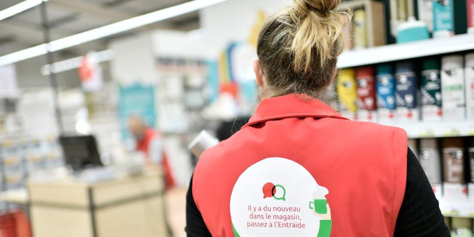 A promotional image inside a Mr Bricolage store, showing an employee from behind, standing in front of rows of DIY equipment