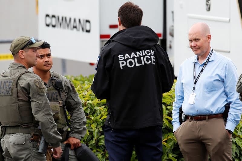 Police officers gather after two armed men entering a bank were killed in a shootout with the police in Saanich