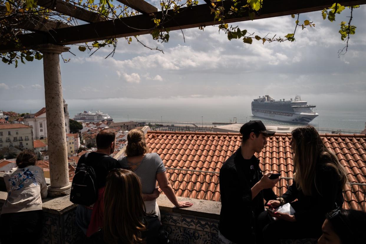 People on a balcony look out at rooftops and a cruise ship