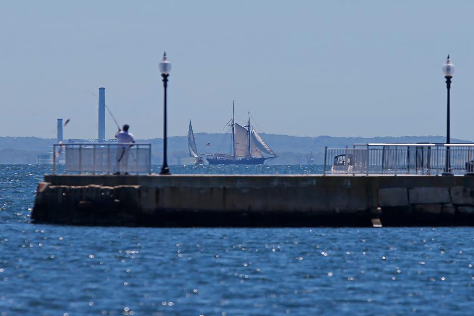 A man chatches a fish off the pier at Fort Taber Park in New Bedford, while in the distance the schooner Ernestina-Morrissey goes for its first sail voyage since returning to New Bedford habor after a long period of restoration in Maine.