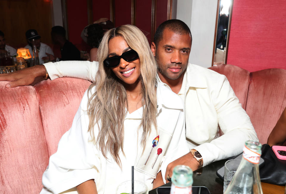 Ciara and Russell Wilson sit close together in a restaurant, both wearing white outfits