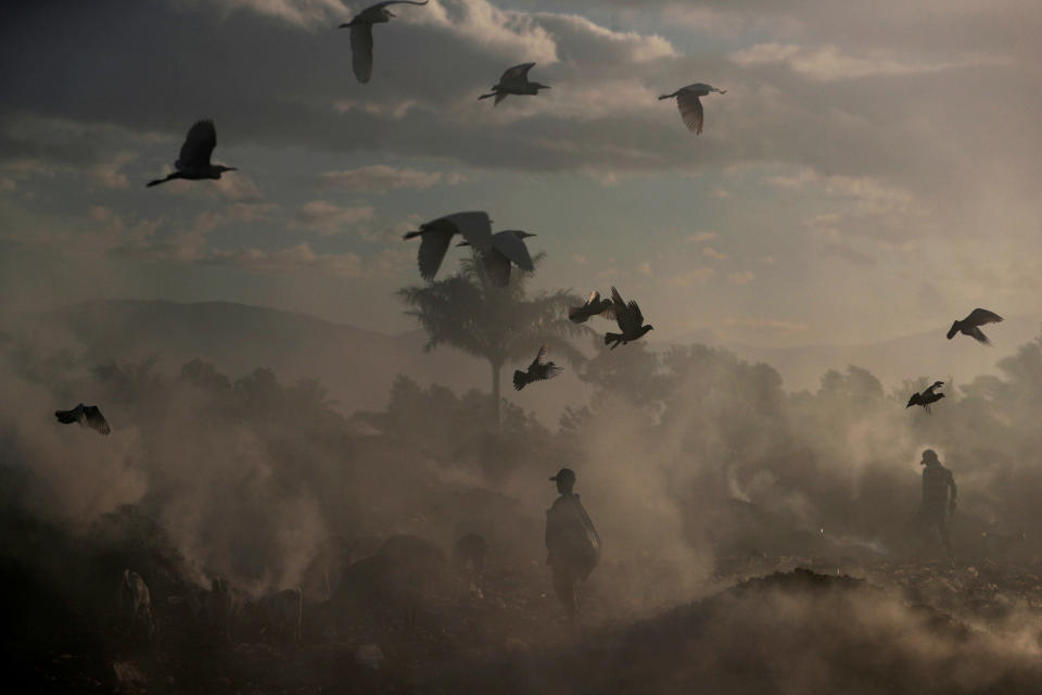 Locals walk among burning rubbish piles at the main garbage dump near Cite Soleil neighbourhood in Port-au-Prince, Haiti, February 21, 2019. Picture taken February 21, 2019.&nbsp;