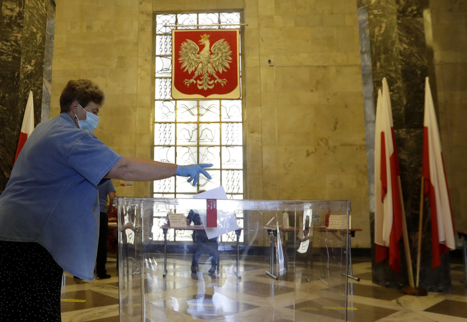 A resident, wearing face mask and protective gloves, casts a vote during presidential election in Warsaw, Poland, Sunday, June 28, 2020. The election will test the popularity of incumbent President Andrzej Duda who is seeking a second term and of the conservative ruling party that backs him. (AP Photo/Petr David Josek)