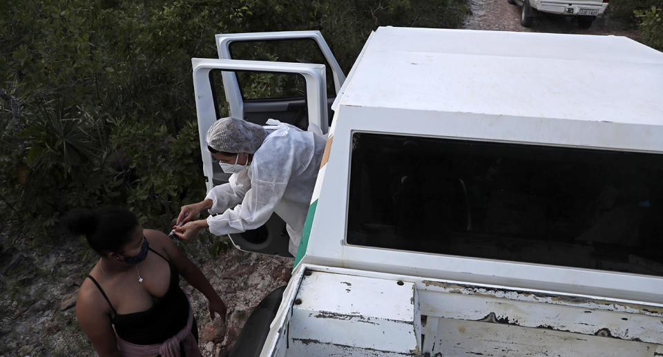 A health worker leans out of a vehicle to give a woman a vaccine.