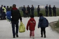 Refugees carry their belongings in front of riot policemen during a police operation at a refugee camp at the border between Greece and Macedonia, near the village of Idomeni, Greece, 24 May 2016. REUTERS/Yannis Kolesidis/Pool