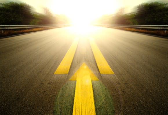 An arrow pointing forward on a road that's leading towards a bright light