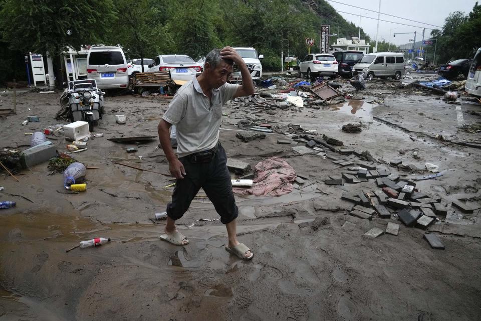 2023年7月31日，北京，連續降雨引發警報，一名男子走過被洪水損壞的車輛和道路。攝：Andy Wong/AP/達志影像