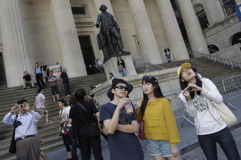 FILE - In this June 15, 2012, file photo, a group of tourists from China take in the sights of the New York Stock Exchange and Federal Hall National Memorial, in New York. With tens of millions of Chinese ordered to stay put and many others opting to avoid travel as the new coronavirus spreads, tourism around the global is taking a heavy hit during one of the biggest travel seasons, the Lunar New Year. (AP Photo/Mary Altaffer, File)