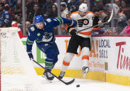 Vancouver Canucks' Riley Stillman, left, checks Philadelphia Flyers' James van Riemsdyk off the puck during the first period of an NHL hockey game Saturday, Feb. 18, 2023, in Vancouver, British Columbia. (Rich Lam/The Canadian Press via AP)