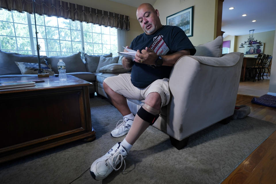 Will Jimeno, the former Port Authority police officer who was rescued from the rubble of the Sept. 11, 2001 attacks at the World Trade Center, reads from "Immigrant, American, Survivor," a children's book he wrote that draws on his experience, during an interview in his home, in Chester, N.J., Monday, Aug. 2, 2021. Injured in the attack, Jimeno wears a compression sock and leg brace band on his left leg. (AP Photo/Richard Drew)