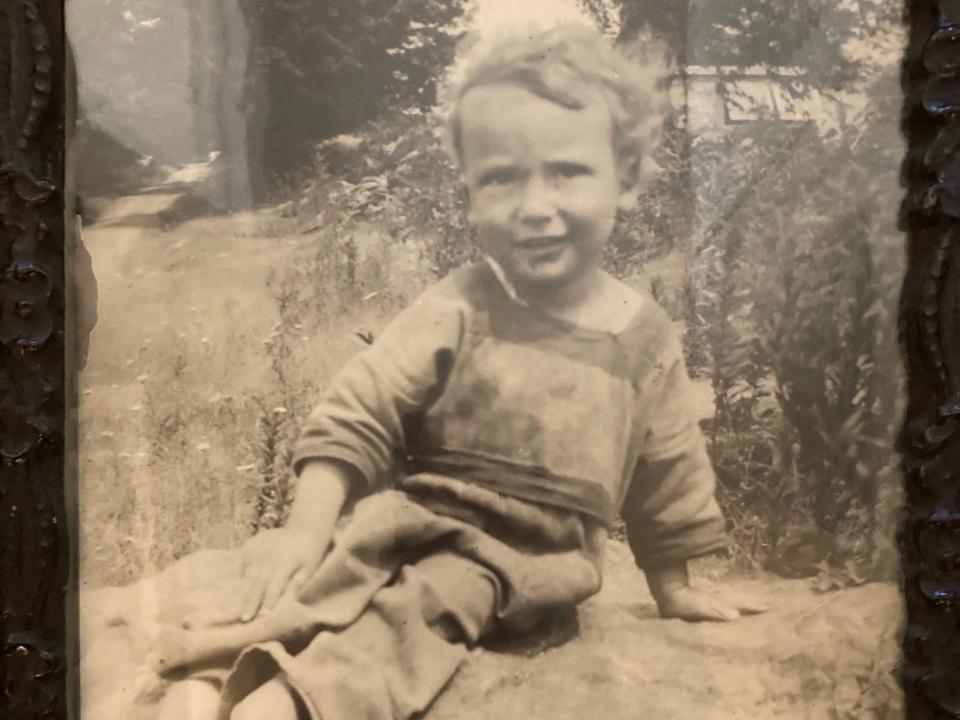 A black and white photo of a little boy sitting on a rock at a farm.