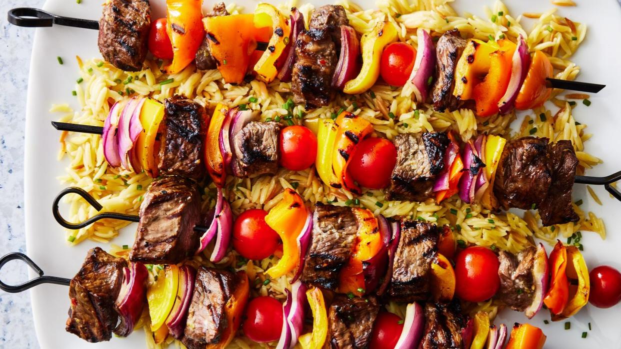 steak kebabs with peppers on top of orzo with a spinach cucumber salad