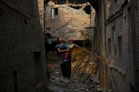 A woman carrying her child stands in an alley surrounded by damaged and collapsed houses following April 25 earthquake at Bhaktapur May 7, 2015. REUTERS/Navesh Chitrakar