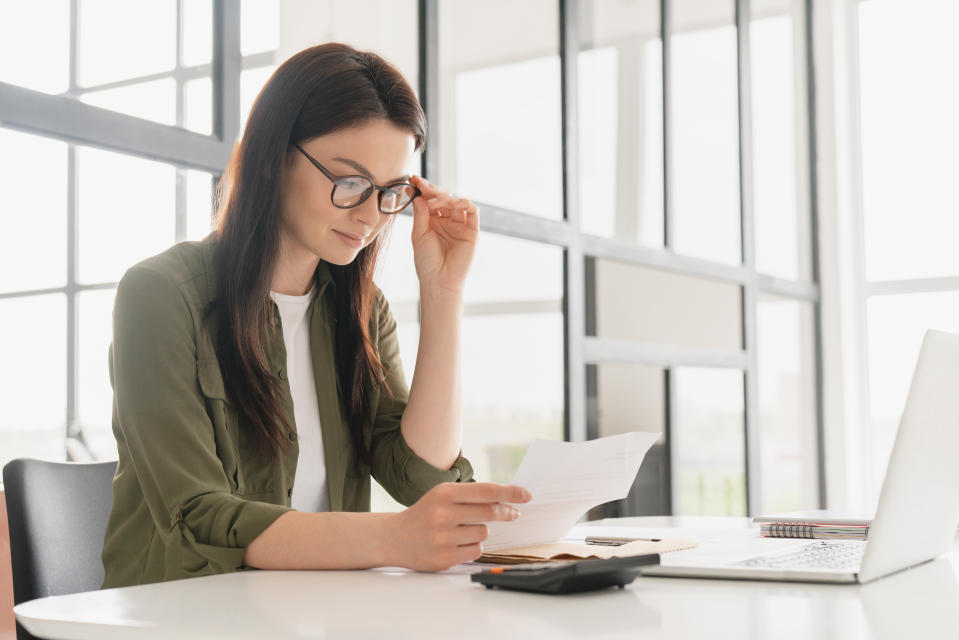 Successful young business woman freelancer manager accountant counting funds, savings, money using calculator in office. Woman paying domestic bills, economizing. Economy and finances concept