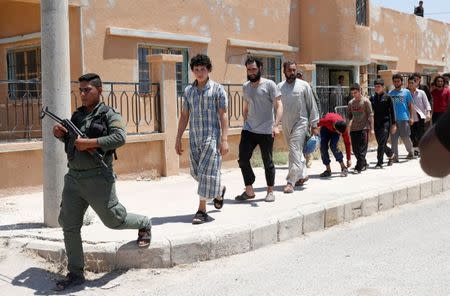 Islamic State prisoners, who were pardoned by a council that is expected to govern Raqqa once the group is dislodged from the Syrian city, walk behind a Kurdish policeman in Ain Issa village, north of Raqqa, Syria June 24, 2017. REUTERS/Goran Tomasevic