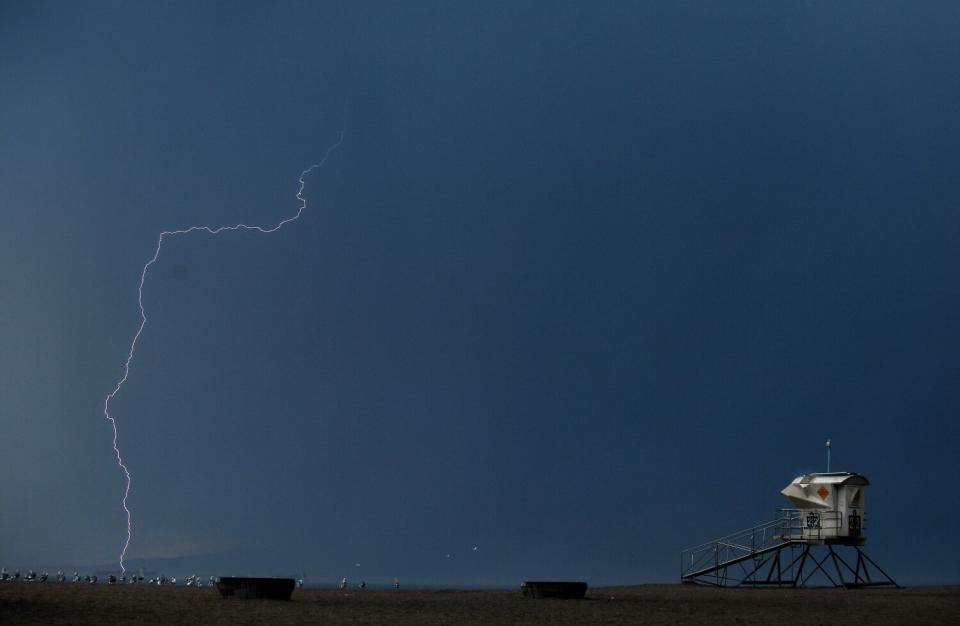 A lightning bolt strikes the ocean near a lifeguard tower at a beach.