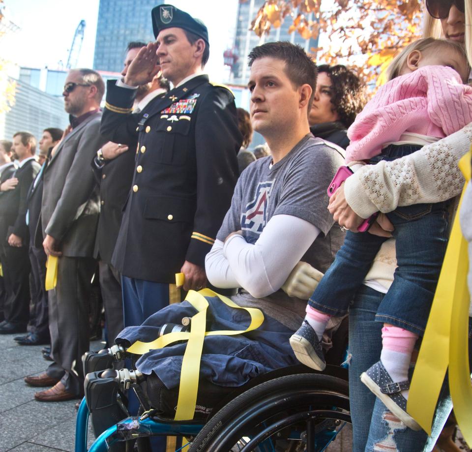 FILE--In this Nov. 10, 2014, file photo, former U.S. Air Force Senior Airman Brian Kolfage, center, sits in a wheelchair next to his wife Ashley, right, who holds their daughter Paris, during the National September 11 Memorial and Museum's "Salute to Service" tribute honoring U.S. veterans in New York. Kolfage, a triple-amputee who lost his limbs serving in Iraq in the U.S. Air Force, started a GoFundMe page to help fund construction of President Donald Trump's border wall has already raised millions of dollars.