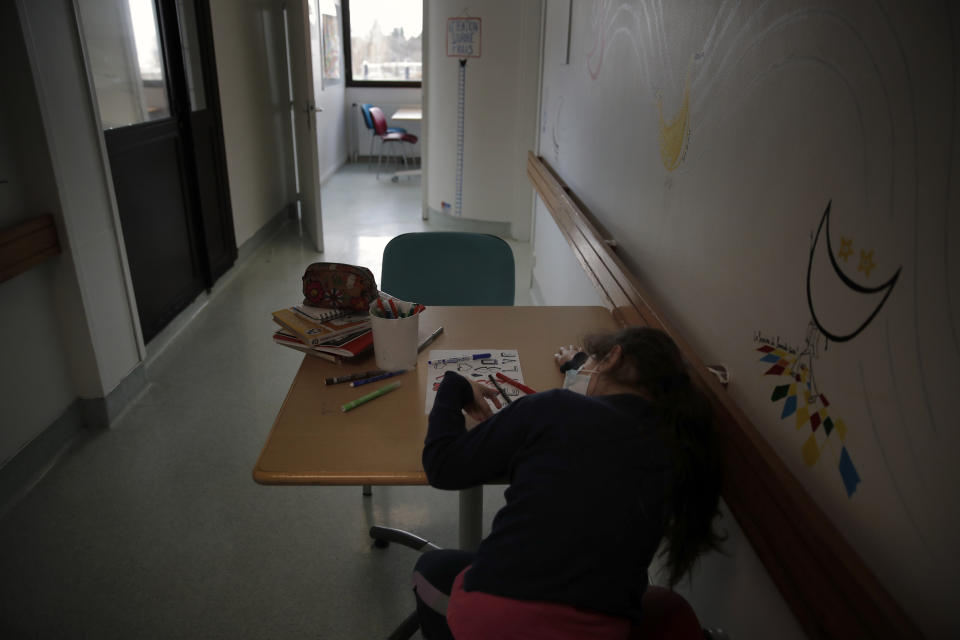 A young girl draws as she sits at a desk inside the pediatric unit of the Robert Debre hospital, in Paris, France, Wednesday, March 3, 2021. (AP Photo/Christophe Ena)