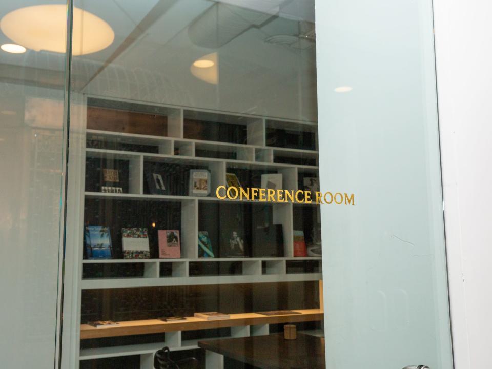 A room surrounded by glass walls with shelves and a "conference room" label on the front door.