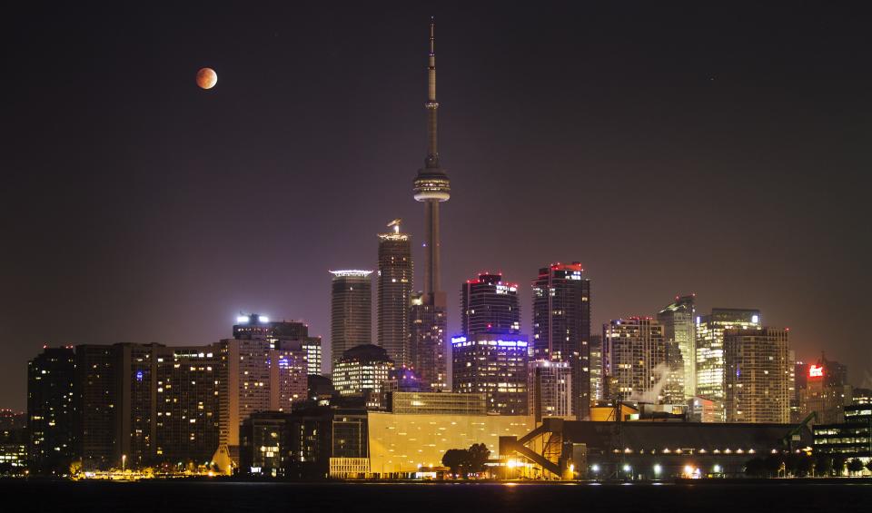 The moon turns orange during a total lunar eclipse behind the CN Tower and the skyline during moonset in Toronto