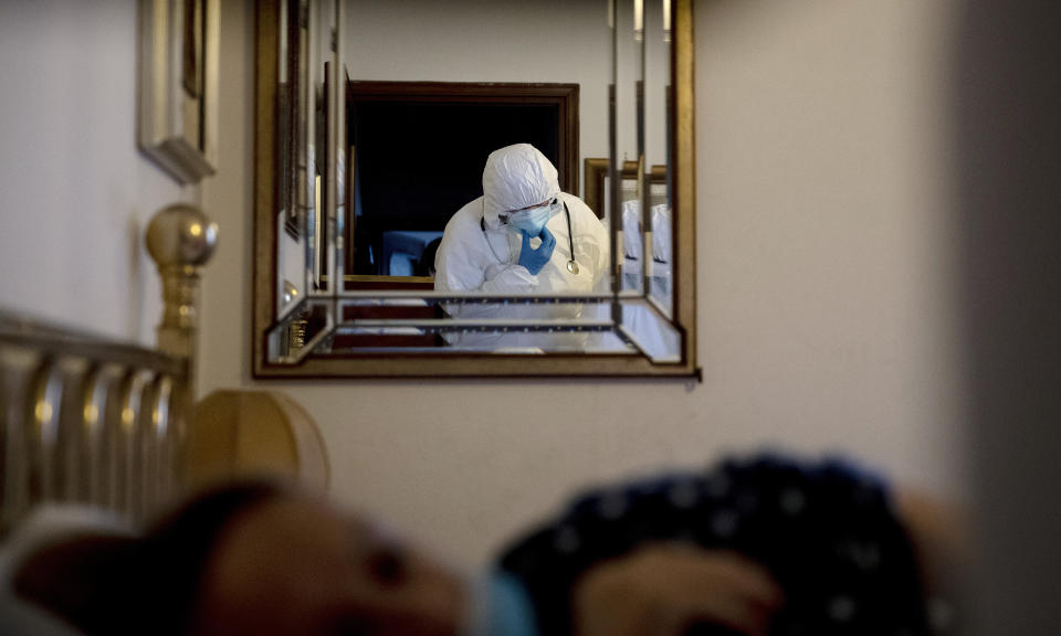 Doctor Luigi Cavanna is reflected in a mirror as he tends to COVID-19 patient Maria Teresa Orsi at her home, in Monticelli D'Ongina, near Piacenza, Italy, Wednesday, Dec. 2, 2020. (AP Photo/Antonio Calanni)