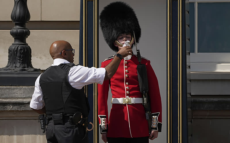 A police officer gives water to a British soldier wearing a traditional bearskin hat, on guard duty outside Buckingham Palace, during hot weather in London on July 18. The government issued its first-ever “red” warning for extreme heat. <em>Associated Press/Matt Dunham</em>