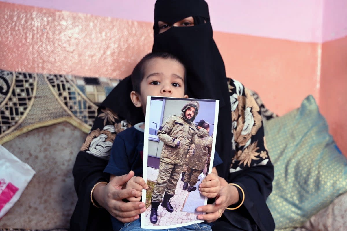 This photo taken on 22 February 2024 shows a picture printout of Indian national Mohammed Asfan, seen wearing Russian military fatigues who last called family from the southern Russian city of Rostov-on-Don before being deployed amid the conflict in Ukraine, being held by his wife Asma Shireen and their child in Hyderabad (AFP via Getty Images)