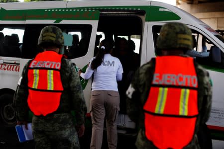 Military police officers observe an immigration agent during a search at a checkpoint on a road in Tapachula