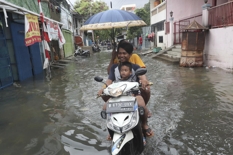 Residents ride a motorbike on a flooded street in Jakarta, Indonesia, Sunday, Jan. 5, 2020. Landslides and floods triggered by torrential downpours have left dozens of people dead in and around Indonesia's capital, as rescuers struggled to search for people apparently buried under tons of mud, officials said Saturday. (AP Photo/Tatan Syuflana)