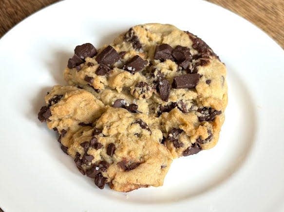 A chocolate-chunk Crumbl cookie on a white plate placed on a wooden table.