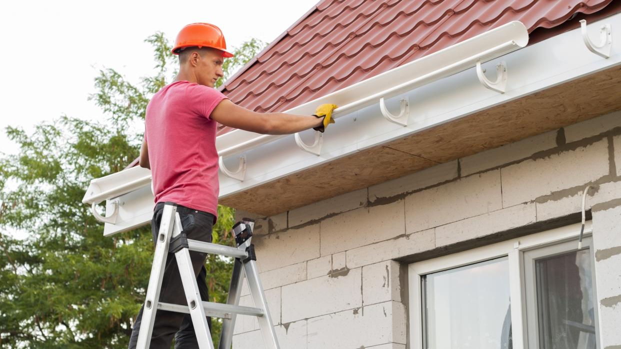 worker installs the gutter system on the roof.