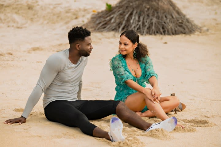 A man and woman stare at each other while sitting on a beach.