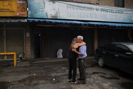 Manuel Fernandes, un comerciante, se abraza con una vecina a las afueras de su panadería luego de que fue saqueada en medio de las protestas en contra del presidente venezolano Nicolás Maduro en la ciudad de Los Teques, cerca de Caracas, Venezuela, 19 de mayo de 2017. REUTERS/Carlos Barria