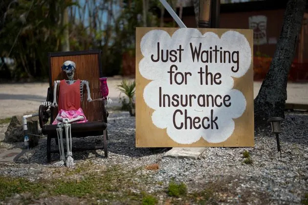 A skeleton in sunglasses sits beside a sign reading 