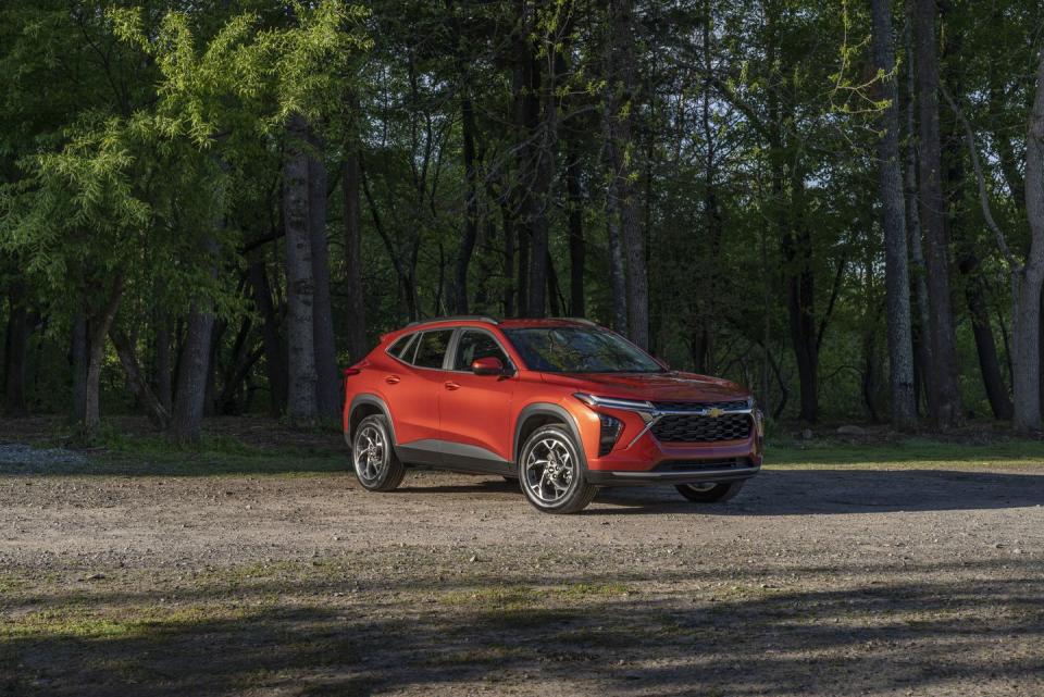 front 34 view of 2024 chevrolet trax lt in cayenne orange metallic parked on a gravel road in front of trees