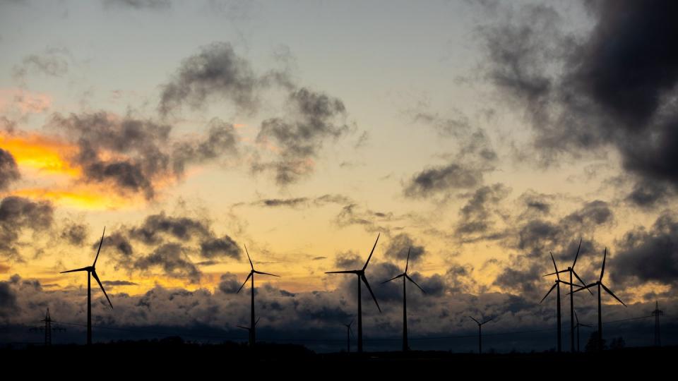 Dunkle Wolken ziehen vor einem orange gefärbtem Himmel über Windräder hinweg.