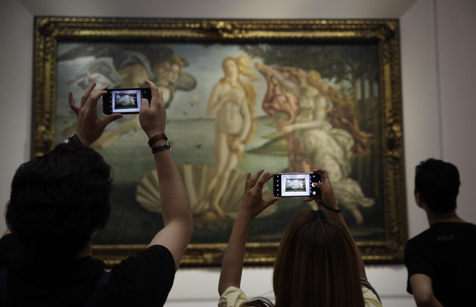 Visitors closely admire early Renaissance painter Sandro Botticelli's "Birth of Venus", at the Uffizi Gallery museum, in Florence, Italy, Tuesday, Aug. 6, 2019. To protect the masterpieces in the Uffizi Gallery’s collection, the Florence museum’s director climbed a ladder and hurled an employee’s bicycle down at a sheet of glass specially made to keep prized pieces such as Botticelli’s “Spring” and “Birth of Venus” safe from vandals. (AP Photo/Luca Bruno)