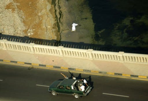 Libyan rebels patrol an area in Tripoli as a dead body floats in the sea